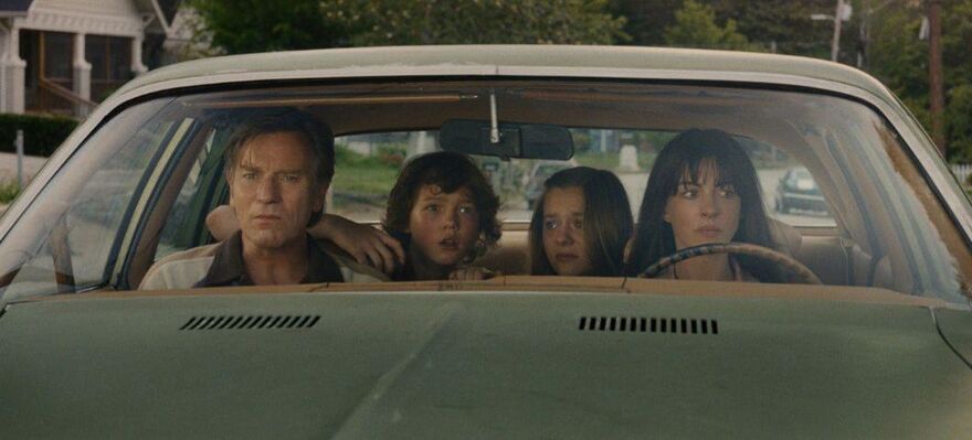 A family of four look concerned within a green car