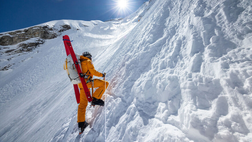 A person in a yellow ski suit climbing up the side of Everest