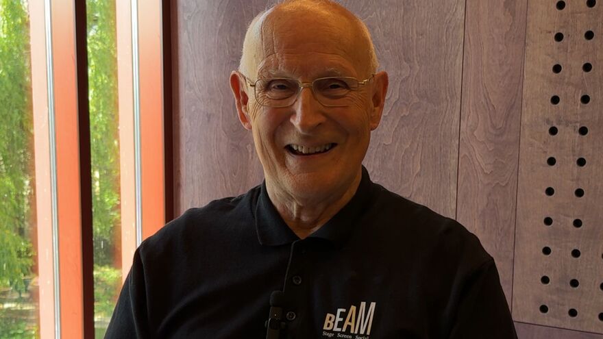 A elderly gentleman sat in front of a window. Smiling warmly in his BEAM top.