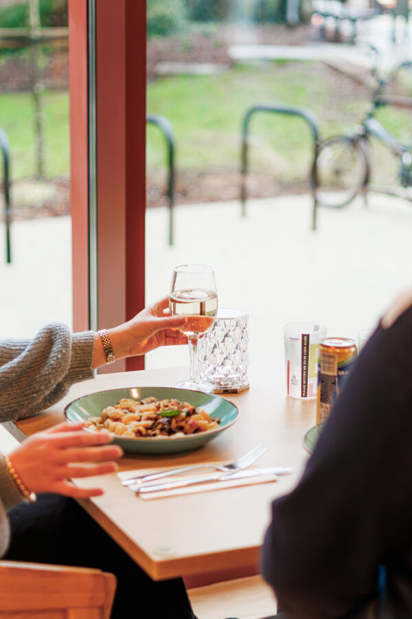 Two people sitting at a table in BEAM's kitchen bar with a bowl of pasta and a glass of wine