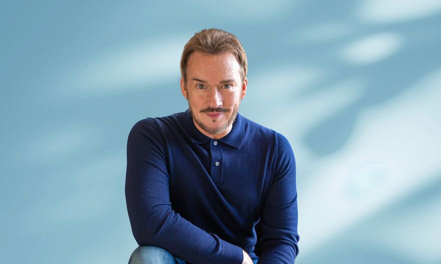 Russell Watson crouching down in a dark blue shirt