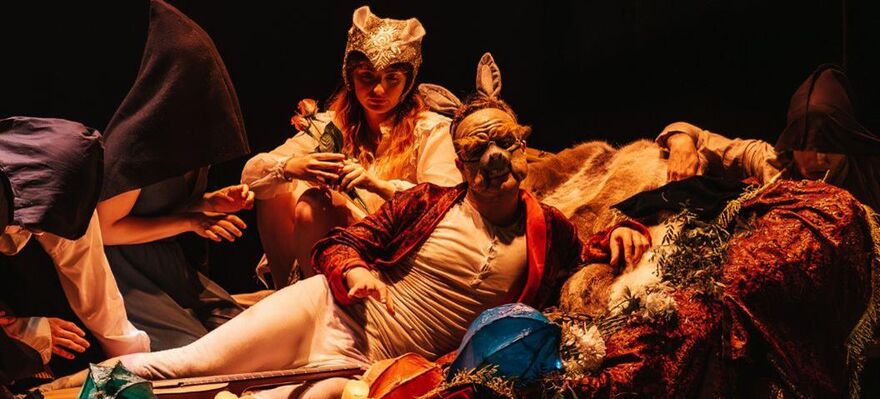 Two cast members lay on set in Shakespearean costume and masks