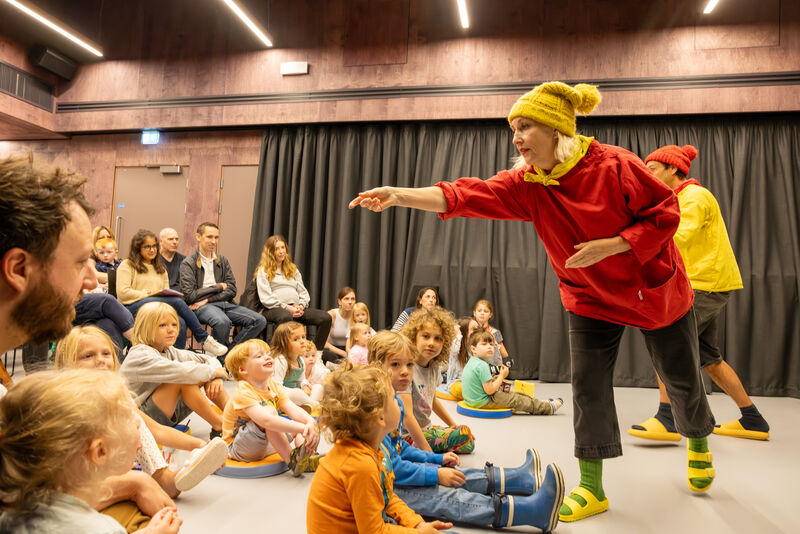 Two facilators in colourful clothing interact with a group of children in a workshop