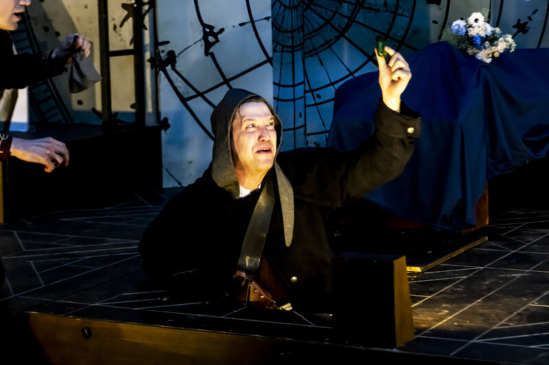 An actor coming up through stage floor holding a bottle