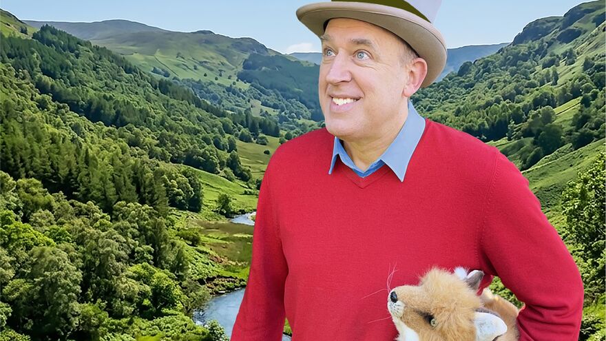 Tim Vine stood in front of a scenic view with a stuffed toy fox
