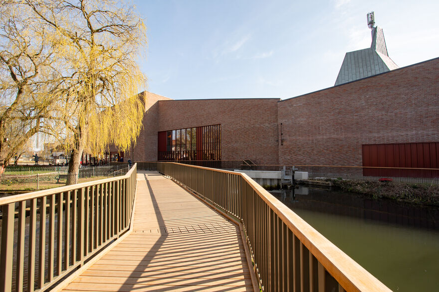 Exterior of BEAM (Venue). Brick walls on a sunny day. Wooden bridge.