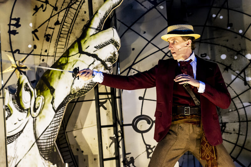 An actor on stage with a sword pointing forward