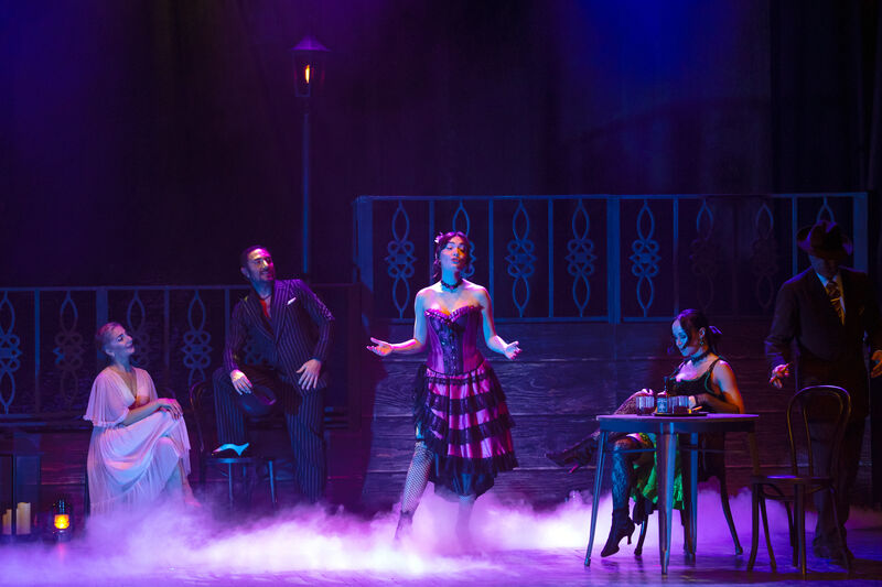 Dancers and a singer on stage in a saloon setting