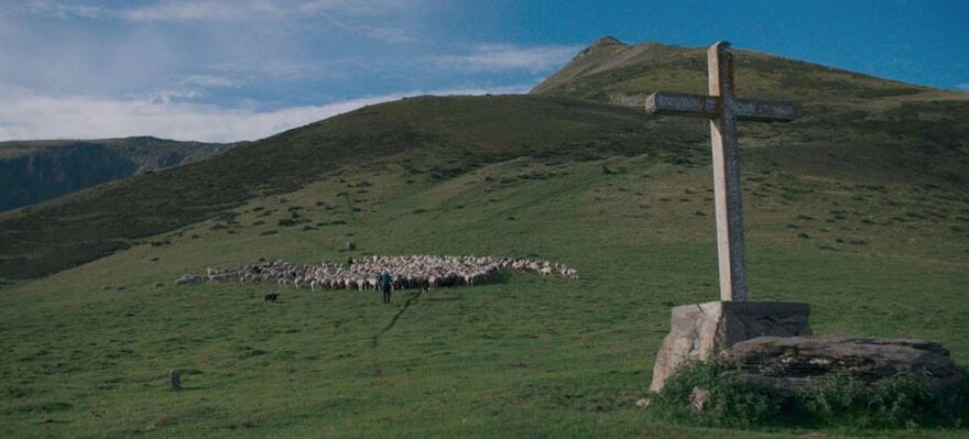 A green mountain scene with a shepherd and his flock of sheep
