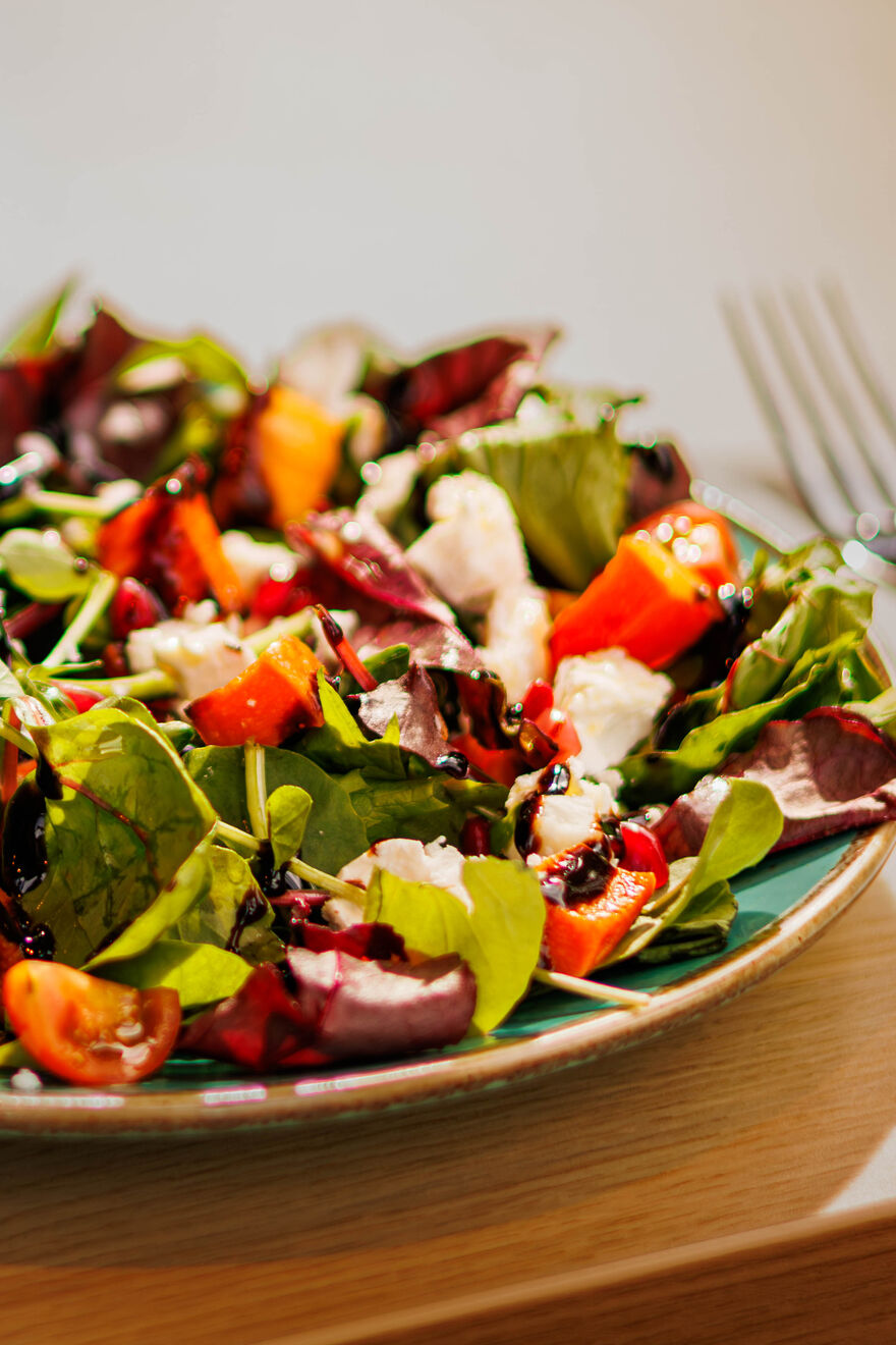 A plate of salad with leaves, tomatoes and feta cheese