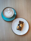 A hot coffee in a blue cup and a slice of cake on a saucer