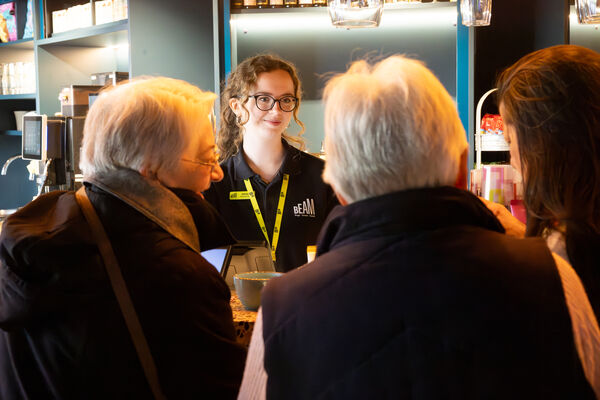 A woman in a BEAM t-shirt assisting three women at the bar 