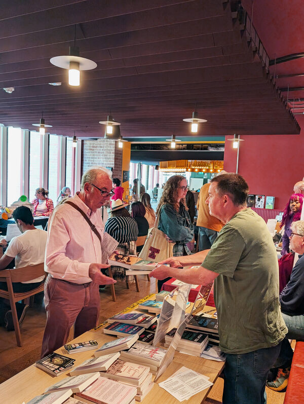 Two men exchange a book in a busy cafe area