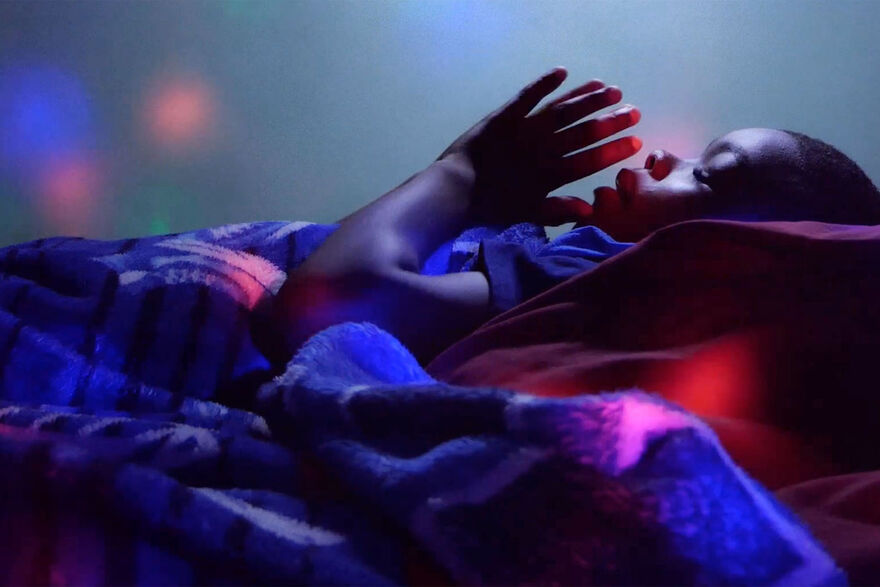 A young boy lays in a blanket with his eyes closed and his hands in prayer