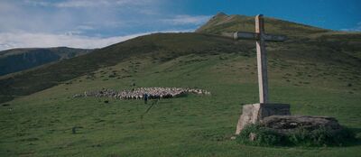 A green mountain scene with a shepherd and his flock of sheep