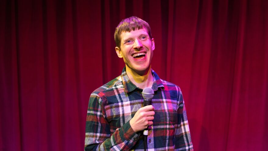 David Eagle in front of a red curtain holding a microphone