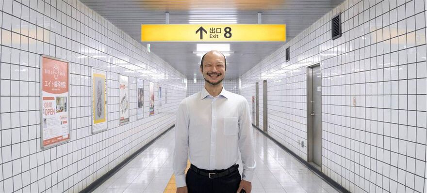 A man stood grinning under an Exit 8 signpost